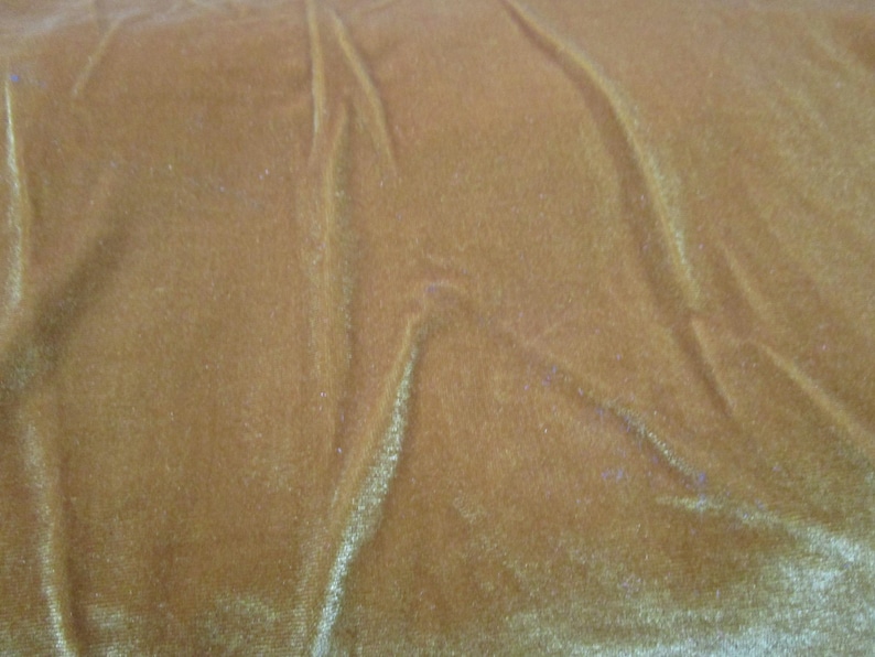 Puede incluir: Primer plano de una tela de terciopelo marr&oacute;n dorado con sutiles reflejos y pliegues. El material suave tiene un brillo lujoso, con luz que se refleja en la superficie texturizada. El color de la tela es un tono c&aacute;lido y acogedor.