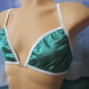 May include: A teal satin bra with white trim and straps. The bra has a triangle cup design and a clear plastic clasp closure. The garment is displayed on a mannequin.