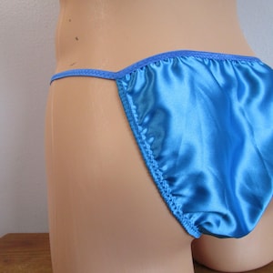 May include: Bright blue satin underwear with a thong back. The edges are trimmed with matching blue stitching. The underwear is displayed on a mannequin.