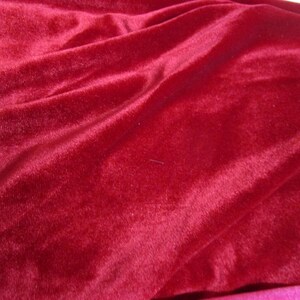 Puede incluir: Primer plano de una tela de terciopelo rojo intenso con pliegues suaves y un brillo lujoso. El material afelpado es de un color rico y s&oacute;lido, ideal para ropa o decoraci&oacute;n del hogar.