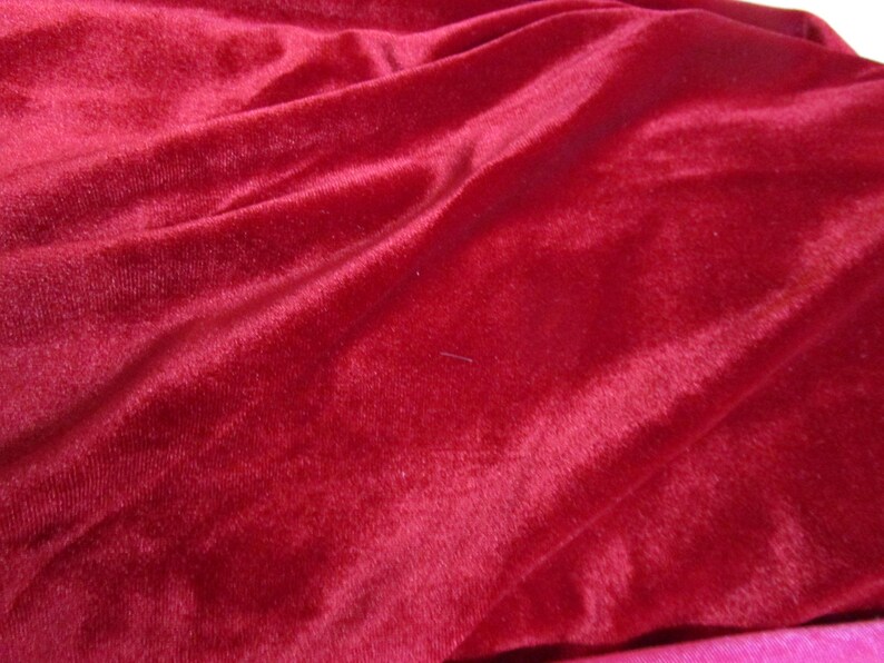 Puede incluir: Primer plano de una tela de terciopelo rojo intenso con pliegues suaves y un brillo lujoso. El material afelpado es de un color rico y s&oacute;lido, ideal para ropa o decoraci&oacute;n del hogar.