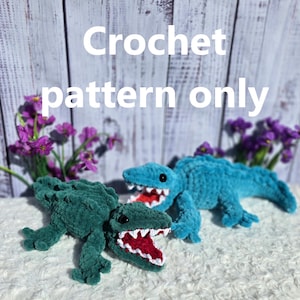 May include: Two crochet alligator toys in teal and green, with white teeth and red mouths. The text "Crochet pattern only" is displayed in white. The toys are on a white, textured surface, with purple flowers in the background.