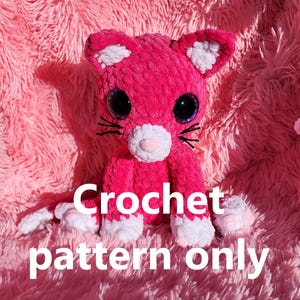 May include: A pink crocheted cat amigurumi toy with white accents and large black eyes. The toy is sitting on a pink fuzzy surface. Crochet pattern only.