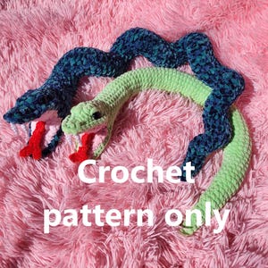 May include: Two crocheted snake toys, one green and one blue, on a pink fuzzy surface. The text "Crochet pattern only" is visible in the image.
