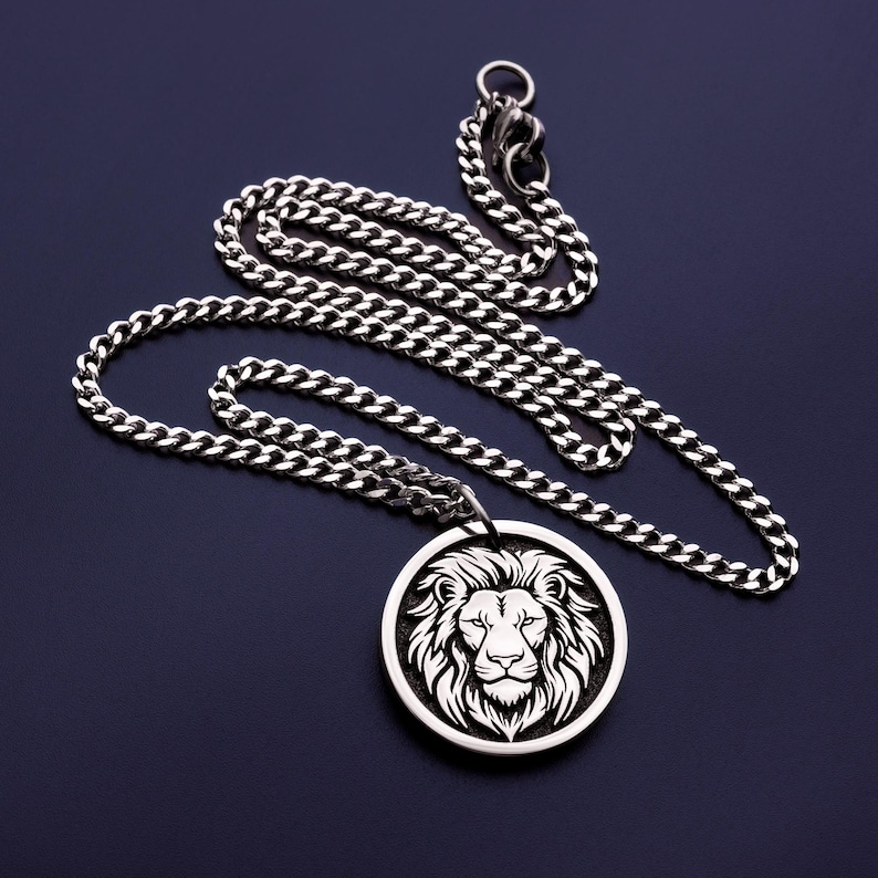 May include: Silver-toned necklace featuring a detailed lion's head pendant. The pendant is circular with a white lion design against a dark background. The chain is a curb style, and the overall aesthetic is bold and masculine.