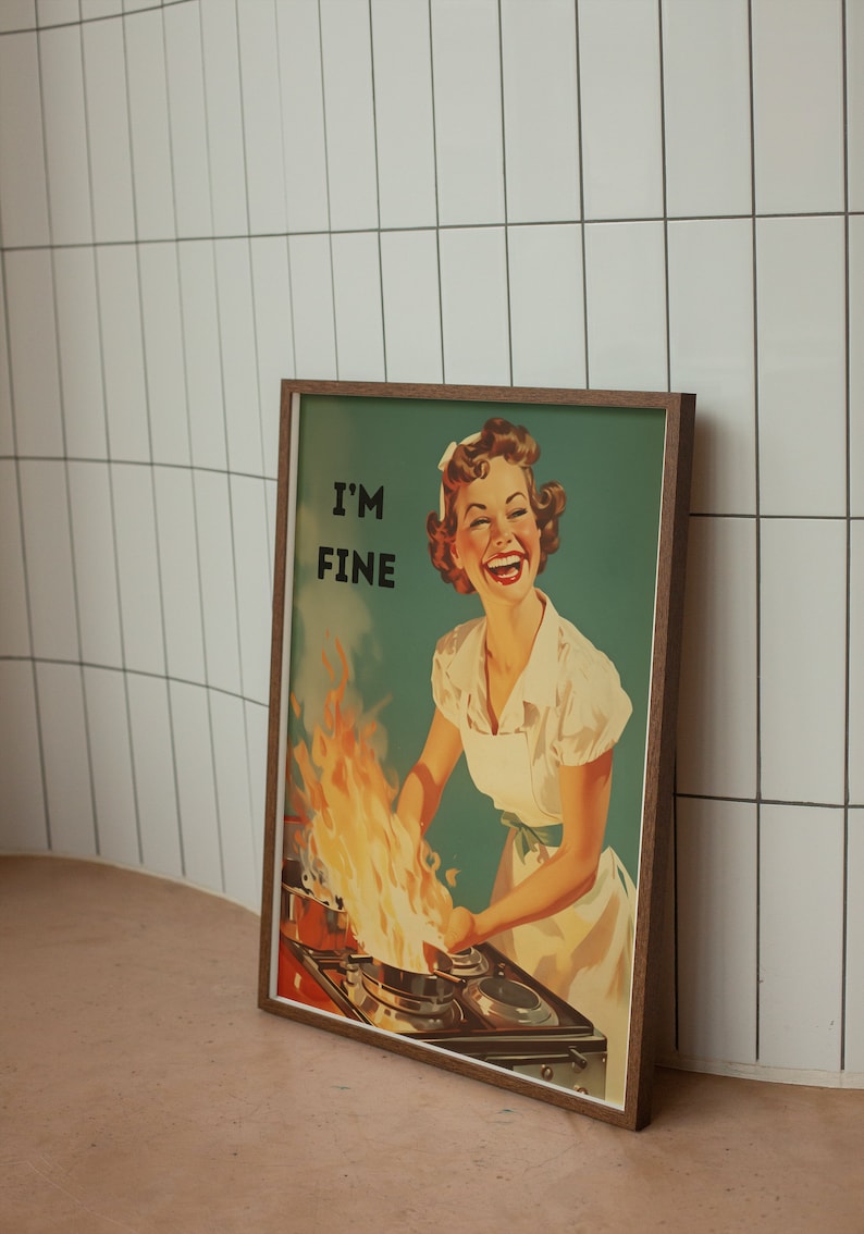 May include: A framed vintage poster with a woman in a white apron standing in front of a stove with a pot on fire. The poster has the text "I'M FINE" in black letters.