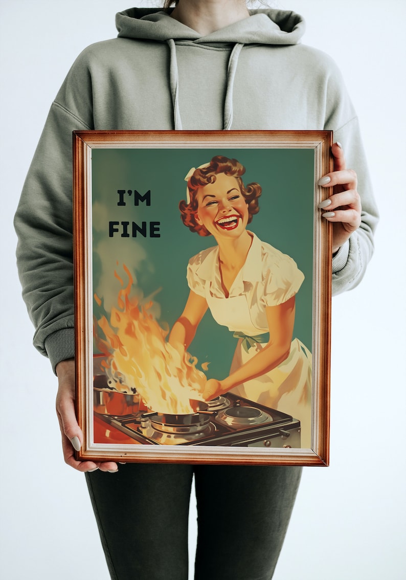 May include: A framed vintage-style poster with a woman in a white dress and apron standing in front of a stove with flames coming from a pan. The text on the poster reads "I'm Fine".