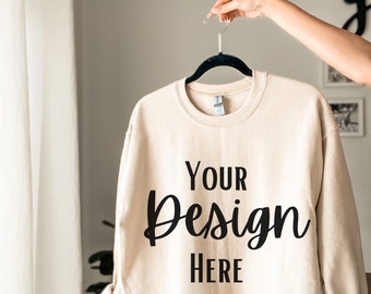 May include: A beige sweatshirt with the text "YOUR Design HERE" printed on the front. The sweatshirt is hanging on a black hanger.