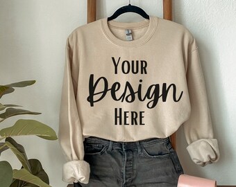 May include: A beige sweatshirt with the text "Your Design Here" on the front. The sweatshirt is hanging on a wooden ladder and is styled with denim shorts and a pink purse.