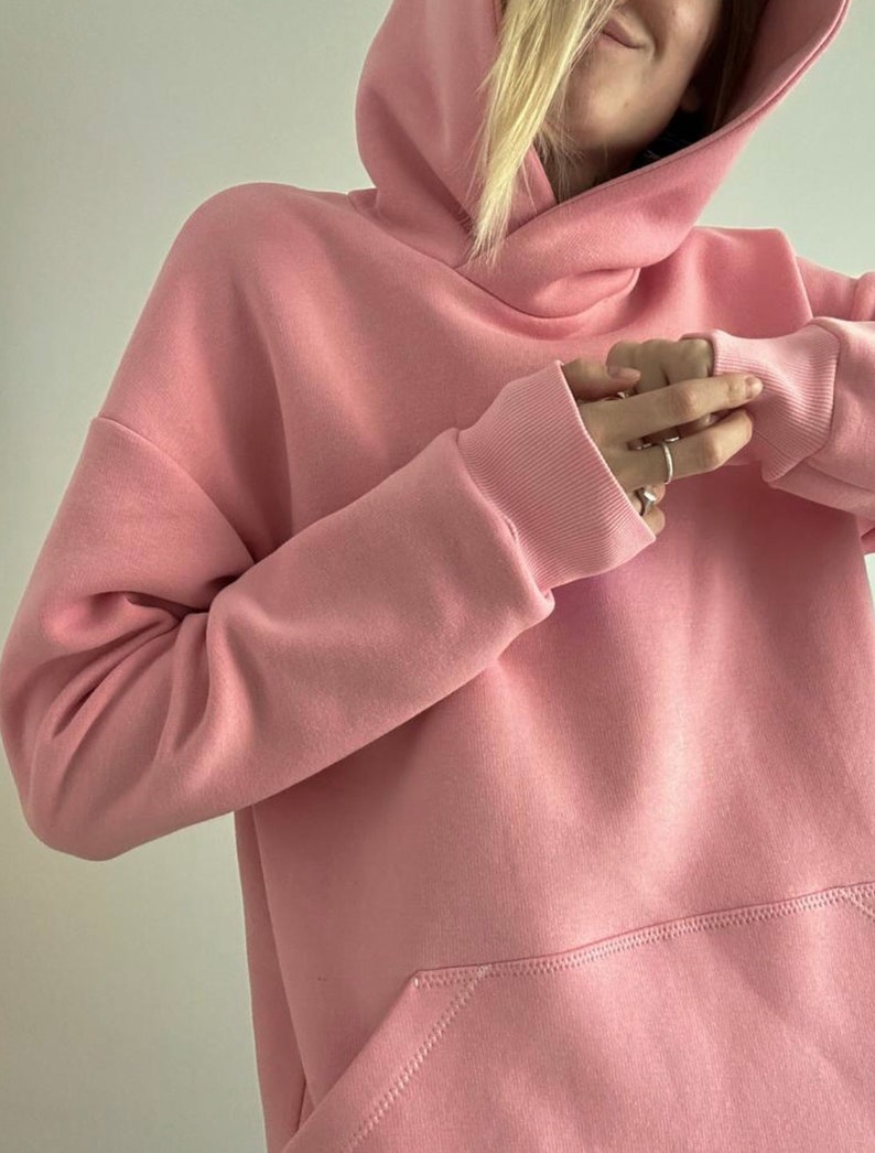 Op de afbeelding: Een roze oversized hoodie met een grote zak aan de voorkant. De hoodie heeft een trekkoord en een losse pasvorm.
