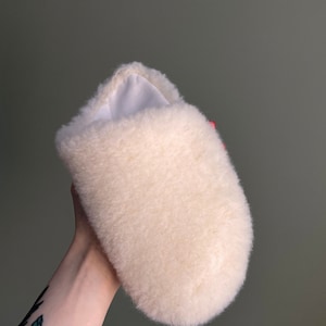 May include: A white fluffy slipper with a soft, plush texture. The slipper is made of a fuzzy material and has a rounded shape.