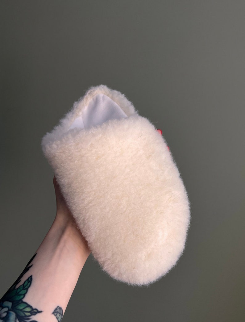 May include: A white fluffy slipper with a soft, plush texture. The slipper is made of a fuzzy material and has a rounded shape.