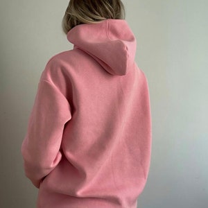 Op de afbeelding: Een roze hoodie met een capuchon met trekkoord.