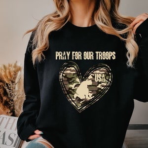 K&ouml;nnte beinhalten: Schwarzes Sweatshirt mit einem Tarnmuster-Herzdesign und dem Text "Pray for our Troops" und "USA".