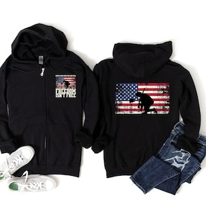 Puede incluir: Sudadera negra con cremallera y capucha, con una bandera americana desgastada en la espalda y el texto "Honor those who paid the price FREEDOM ISN'T FREE" en la parte delantera.