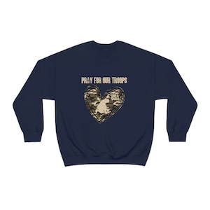 K&ouml;nnte beinhalten: Marineblauer Sweatshirt mit einem Tarnmusterherz und dem Text "Pray for our Troops" und "USA" in Wei&szlig;.