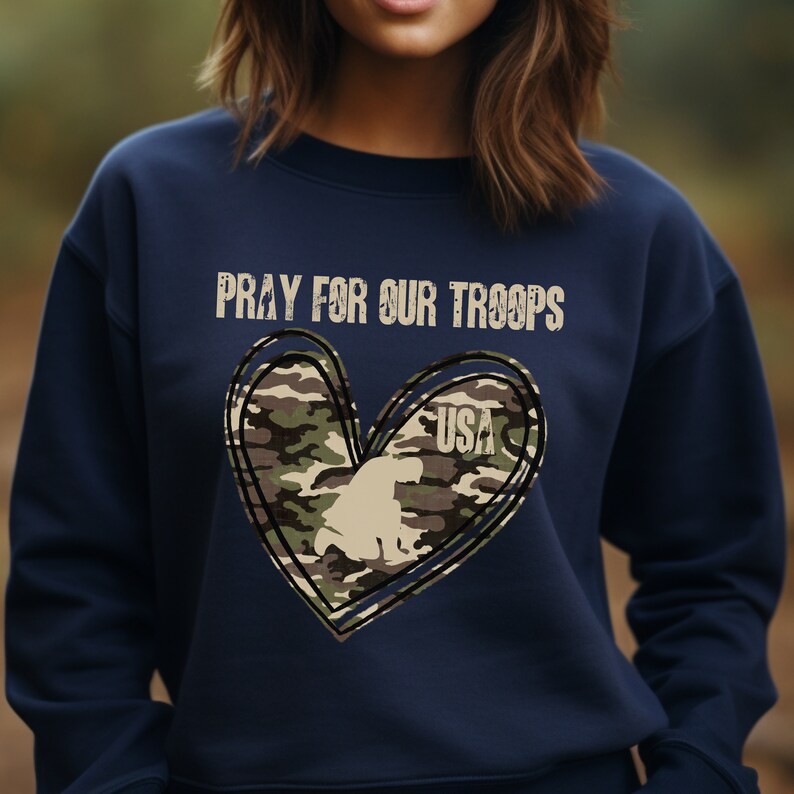 K&ouml;nnte beinhalten: Marineblauer Pullover mit einem Tarnmuster-Herzdesign und dem Text "Pray for our Troops" und "USA".