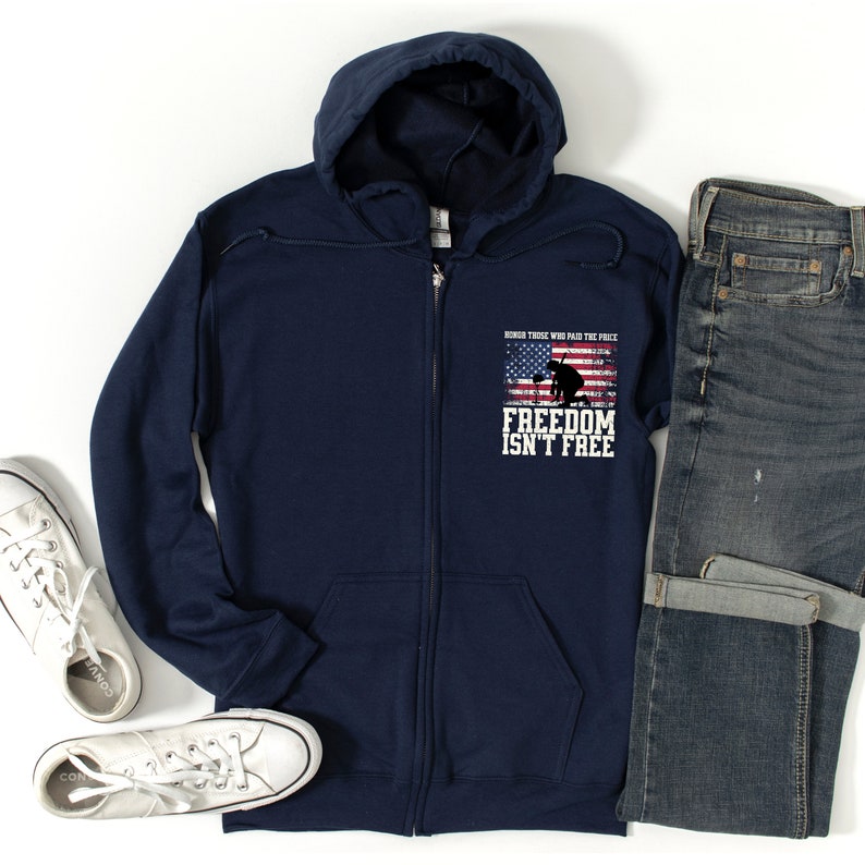 Puede incluir: Sudadera con capucha azul marino con cremallera, con una bandera estadounidense desgastada y una silueta de un soldado arrodillado. El texto "Honor those who paid the price FREEDOM ISN'T FREE" est&aacute; impreso en la sudadera.