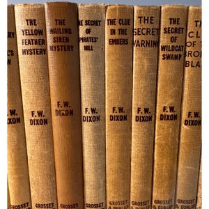 May include: A collection of vintage hardcover books with tan covers. Titles include "The Yellow Feather Mystery," "The Wailing Siren Mystery," and "The Secret of Pirates' Hill." The author's name, F.W. Dixon, is printed on the spines.