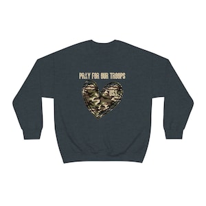 K&ouml;nnte beinhalten: Ein dunkelblauer Pullover mit dem Text "Pray for our Troops" und einem Tarnmusterherz mit dem Wort "USA" darin.