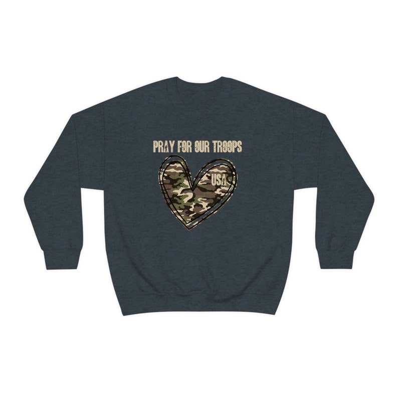 K&ouml;nnte beinhalten: Ein dunkelblauer Pullover mit dem Text "Pray for our Troops" und einem Tarnmusterherz mit dem Wort "USA" darin.