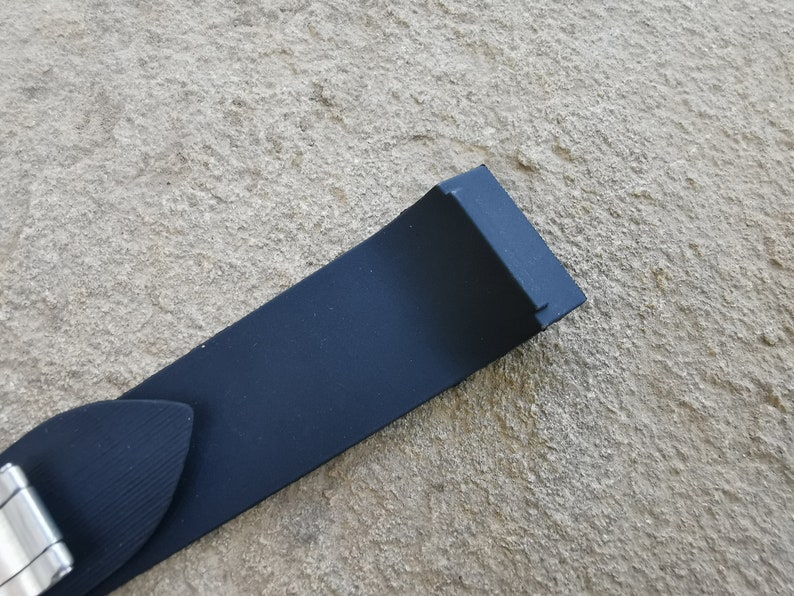 Puede incluir: Primer plano de una correa de reloj azul marino con una hebilla plateada. La correa est&aacute; hecha de un material liso y mate. La correa del reloj mide aproximadamente 2,5 cm de ancho.