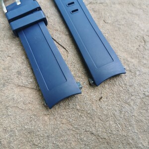Pu&ograve; includere: Due cinturini per orologio blu scuro con barre a molla in metallo. I cinturini sono realizzati in un materiale simile alla gomma.