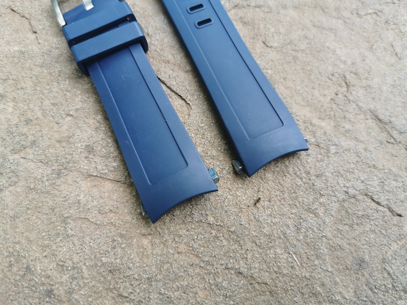 Pu&ograve; includere: Due cinturini per orologio blu scuro con barre a molla in metallo. I cinturini sono realizzati in un materiale simile alla gomma.