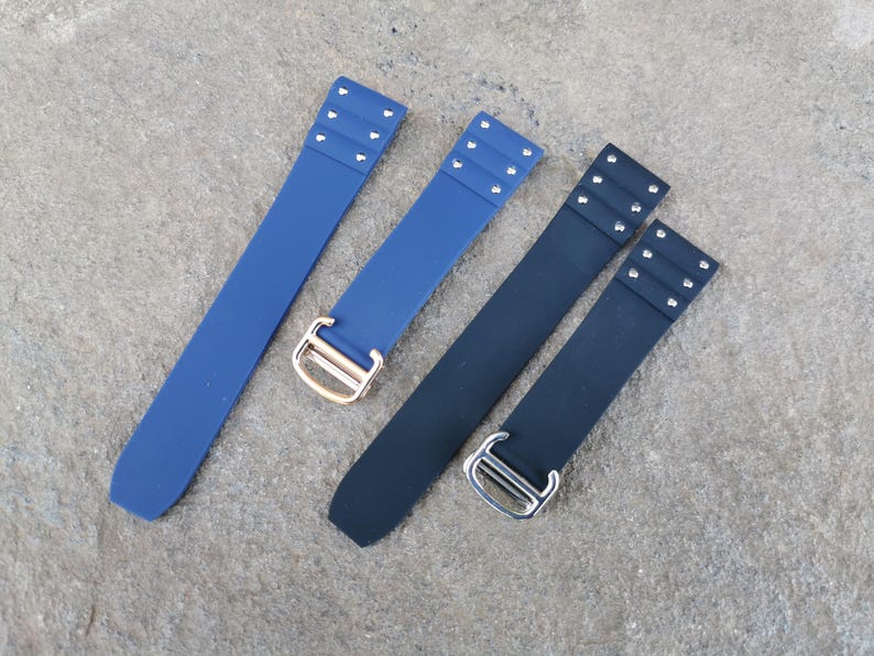 May include: Four watch straps in shades of blue and black. Two are a deep navy blue, and two are a lighter blue. Each strap has a buckle and three small rivets at the end.