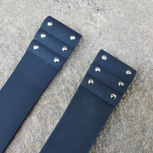 May include: Two navy blue leather straps with silver rivets. Each strap has three rows of rivets. The straps are on a textured, gray surface.