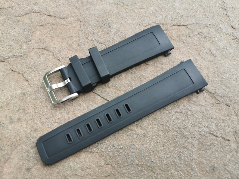 Pu&ograve; includere: Due cinturini per orologio in silicone nero con fibbie argentate. Un cinturino ha una superficie liscia e l'altro ha una fila di fori.