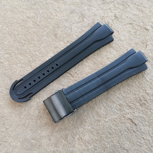 May include: Two black rubber watch straps with a buckle closure. The straps have a textured design and are designed for a watch.