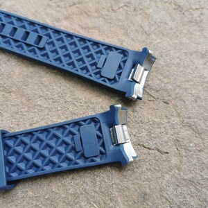 Pu&ograve; includere: Due cinturini per orologio in gomma blu con fibbie in metallo argentato. I cinturini hanno un motivo a rombi.