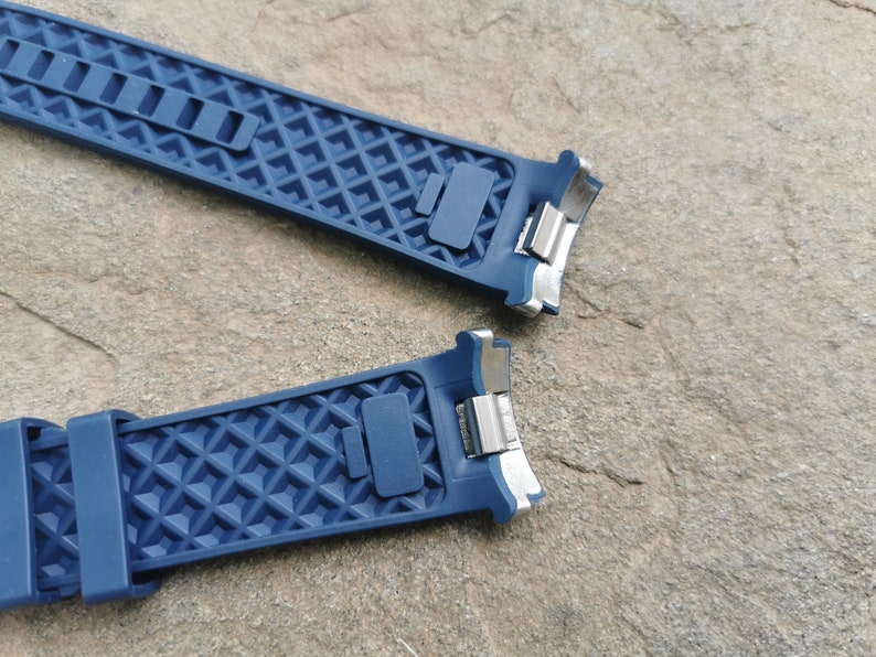 Pu&ograve; includere: Due cinturini per orologio in gomma blu con fibbie in metallo argentato. I cinturini hanno un motivo a rombi.
