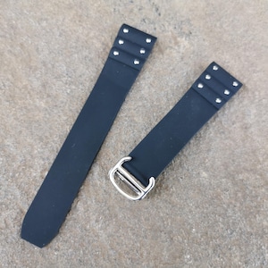 May include: Two-piece black watch strap with silver-tone hardware. Each strap section has three pairs of silver rivets. The strap has a rectangular shape and is made of a smooth, matte material.