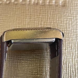 K&ouml;nnte beinhalten: Eine goldfarbene Armbanduhr mit einem braunen Lederarmband. Das Zifferblatt der Uhr ist auf dem Bild nicht zu sehen.