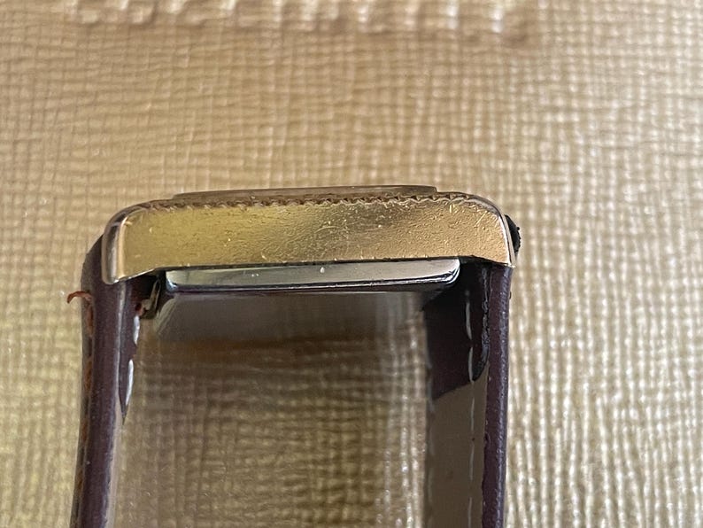 K&ouml;nnte beinhalten: Eine goldfarbene Armbanduhr mit einem braunen Lederarmband. Das Zifferblatt der Uhr ist auf dem Bild nicht zu sehen.