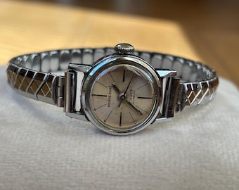 May include: A silver wristwatch with a white face and black hands. The watch has a silver metal band with a checkered pattern. The face of the watch says "Pierre Dore" and "17 Jewels Incabloc".