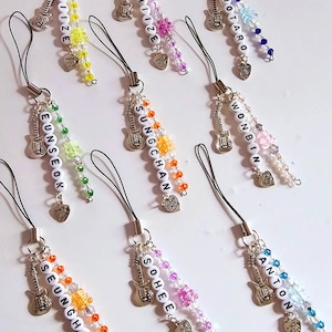 May include: Nine colorful phone charms with different names on each. Each charm has a silver guitar charm, silver heart charm, and beads in various colors. The names on the charms are: Brizie, Shotaro, Wonbin, Sungchan, Eunseok, Sohee, Seunghan, and Anton.
