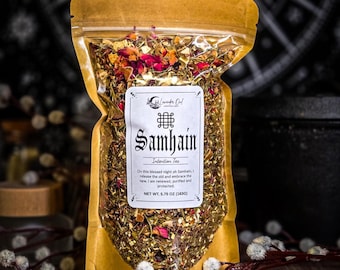 Op de afbeelding: Een doorzichtige stazak gevuld met een losse kruidentheemix met gedroogde rozenblaadjes en kruiden. Het witte etiket bevat de tekst Samhain Intention Tea en vermeldt een nettogewicht van 163g (5,75 oz) met een gedrukte zegening.