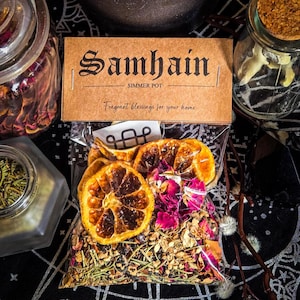 May include: A clear plastic pouch containing a Samhain simmer pot blend with dried orange slices, pink rose petals, and various herbs. The brown paper header features the text Samhain, SIMMER POT, and Fragrant blessings for your home.
