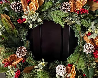 May include: A festive Christmas wreath with a dark background. The wreath is adorned with green pine needles, red berries, dried orange slices, cinnamon sticks, pine cones, and brown magnolia leaves. A seasonal decoration for the holidays.