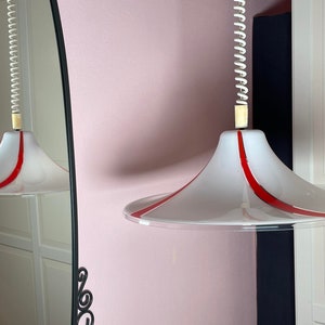 May include: Two white pendant lights with red stripes hang from a ceiling. The lights are suspended by a coiled cord.