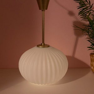 May include: A white, ribbed glass pendant light fixture with a gold metal base and stem.
