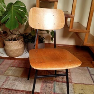 May include: A wooden chair with a black metal frame. The chair has a light brown wood seat and back. The chair is sitting on a patterned rug.