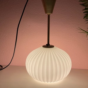May include: A white, ribbed glass pendant light fixture with a gold metal base and a black cord.