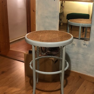 May include: A light blue stool with a woven wicker seat and a metal frame. The stool has a round seat and three legs.