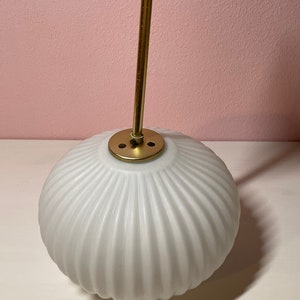 May include: A white, ribbed glass globe pendant light fixture with a gold metal hanging rod and a gold metal canopy.