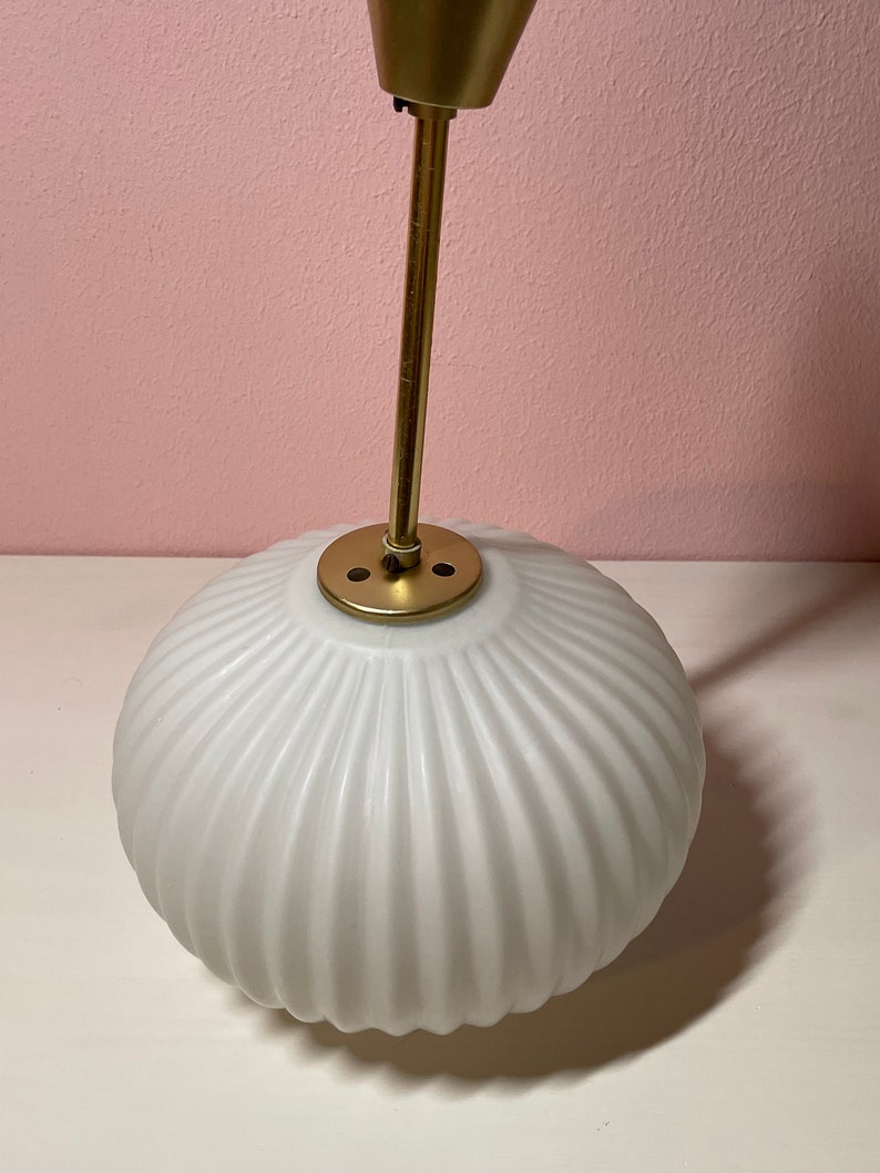 May include: A white, ribbed glass globe pendant light fixture with a gold metal hanging rod and a gold metal canopy.