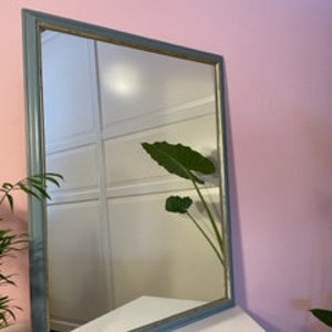 May include: A rectangular mirror with a light blue frame. The frame has a slightly distressed look and a gold trim.
